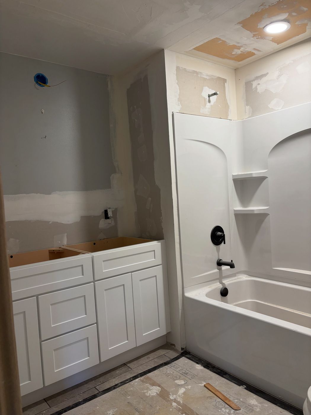 Bathroom mid-remodel with new white shaker vanity and tub surround